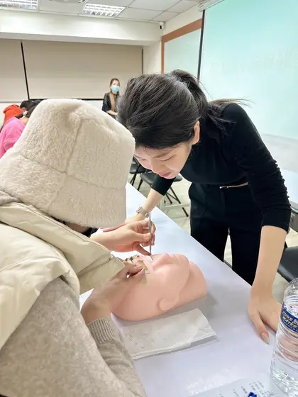 美睫老師彎腰指導學員在假人頭上練習接睫毛